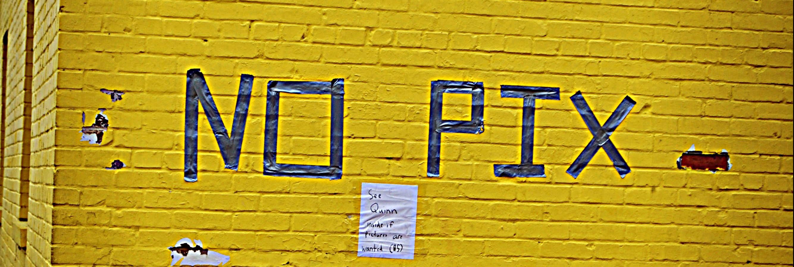 "No Pix" grafiti art on a yellow brick wall